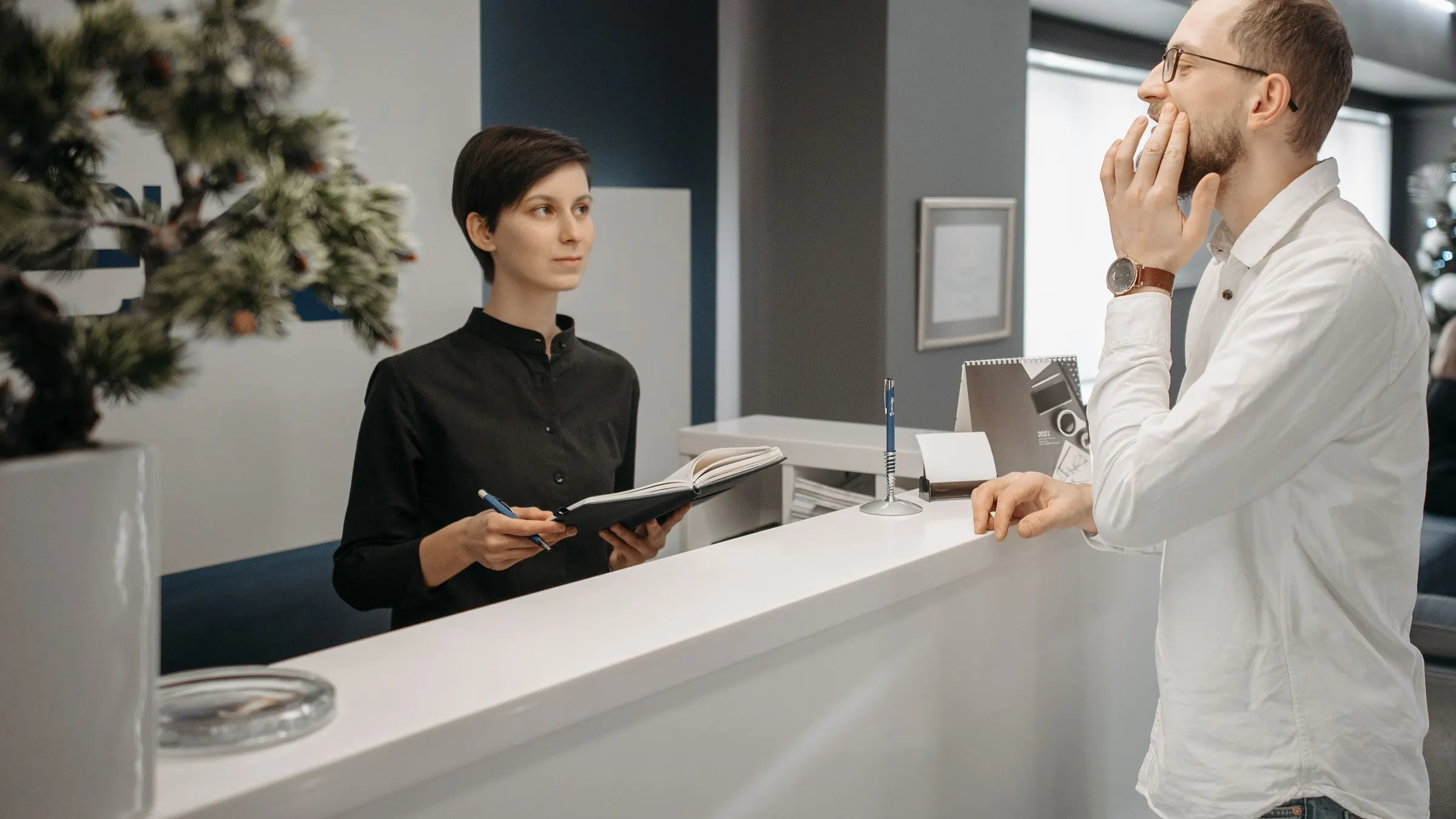 A clinic reception desk with an appointment book and a wall calendar, morning light.