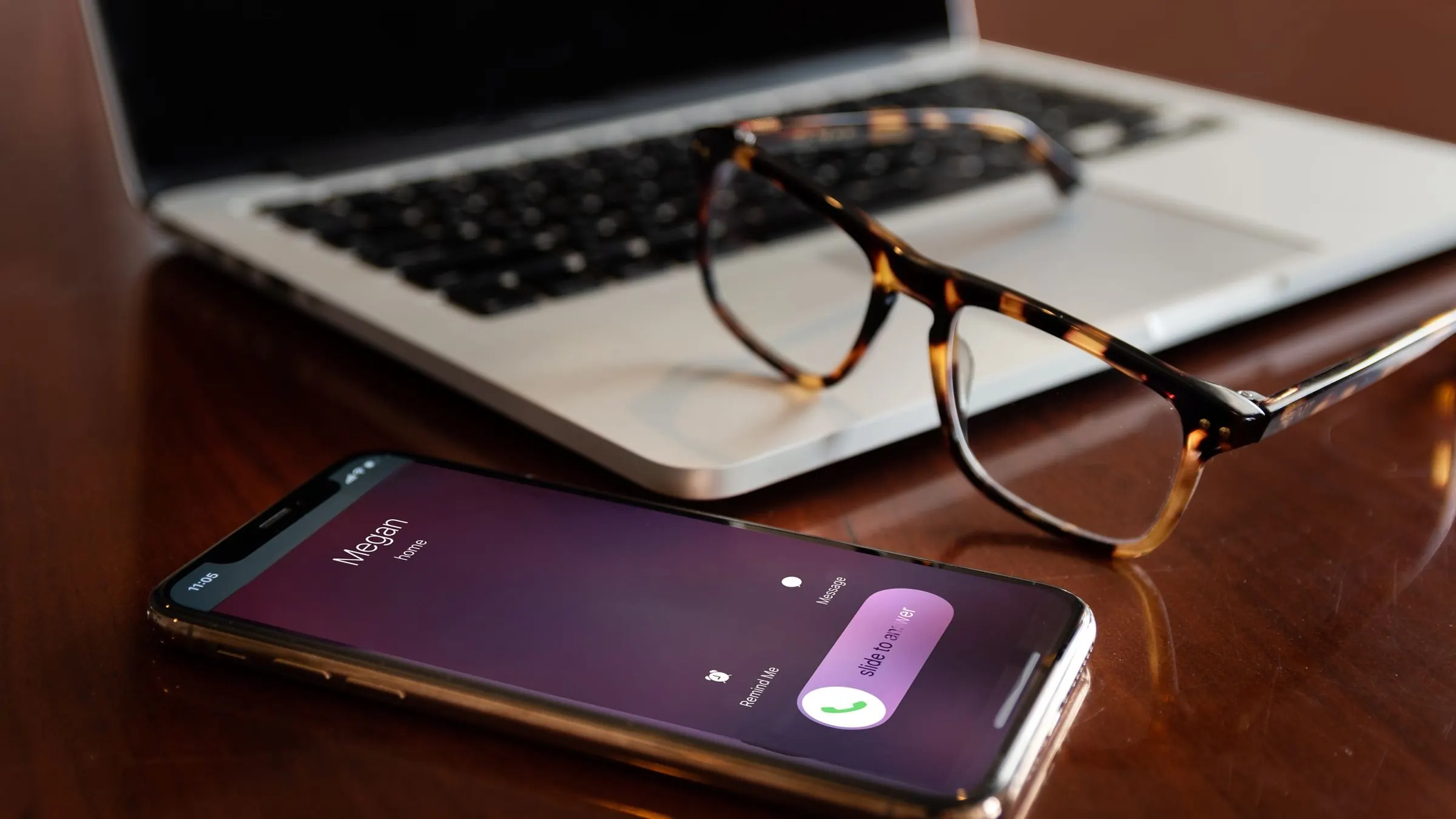 A phone ringing unanswered on a wooden desk, laptop and glasses blurred behind.