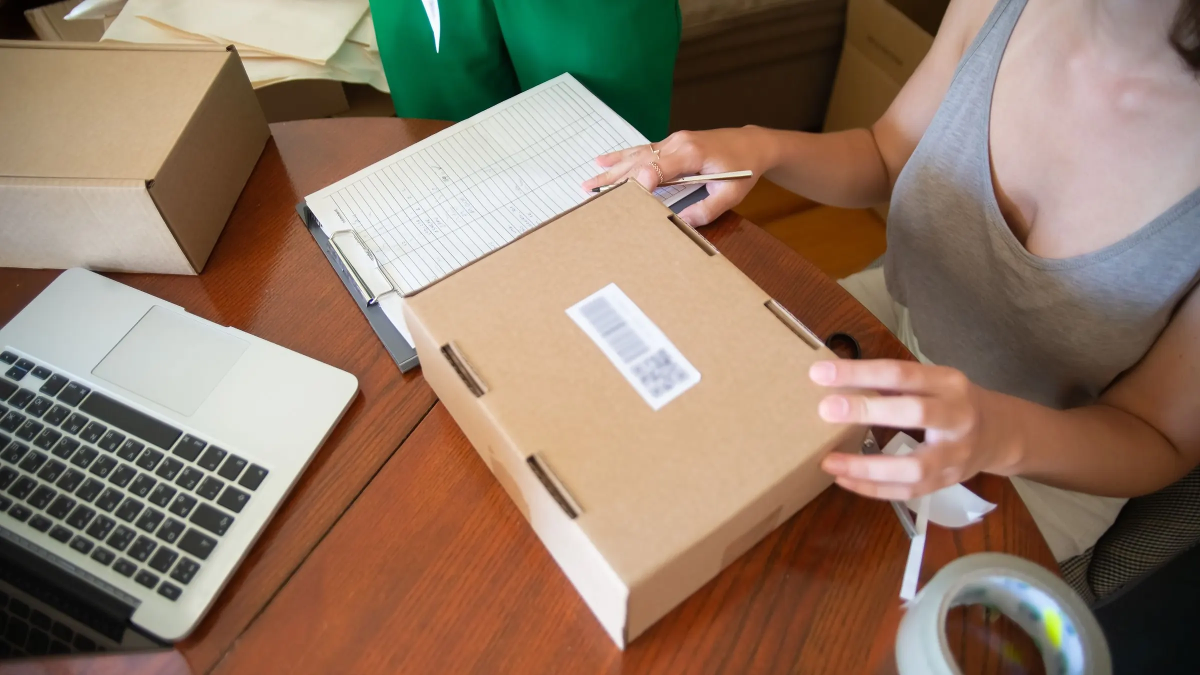An overhead view of a packing table with brown parcels, tape, and a laptop.